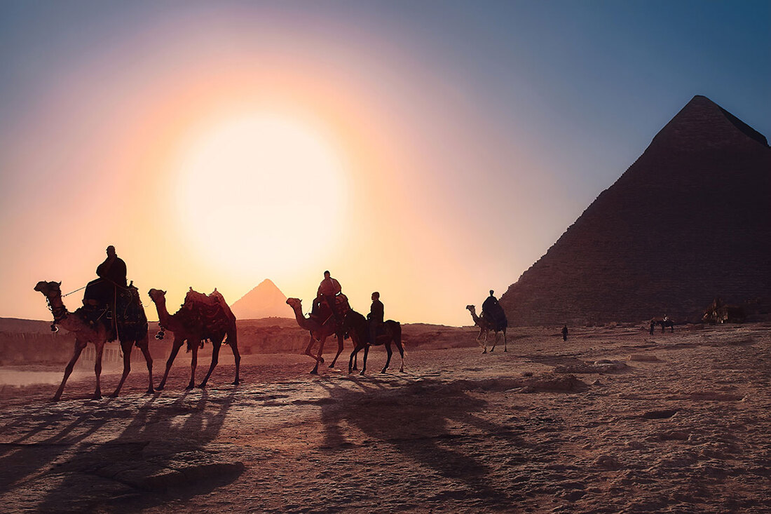 People riding camels in front of the pyramids of Egypt