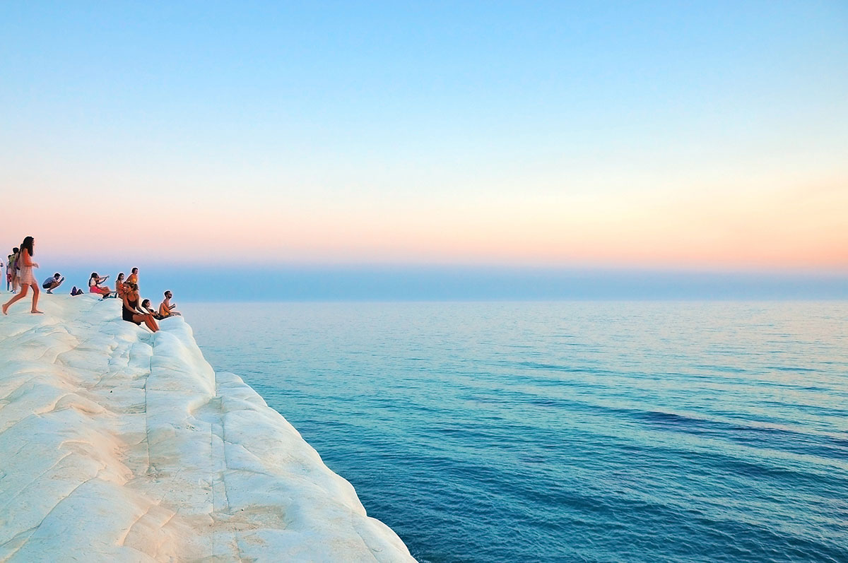 People sitting on a limestone shelf overlooking the ocean in Italy